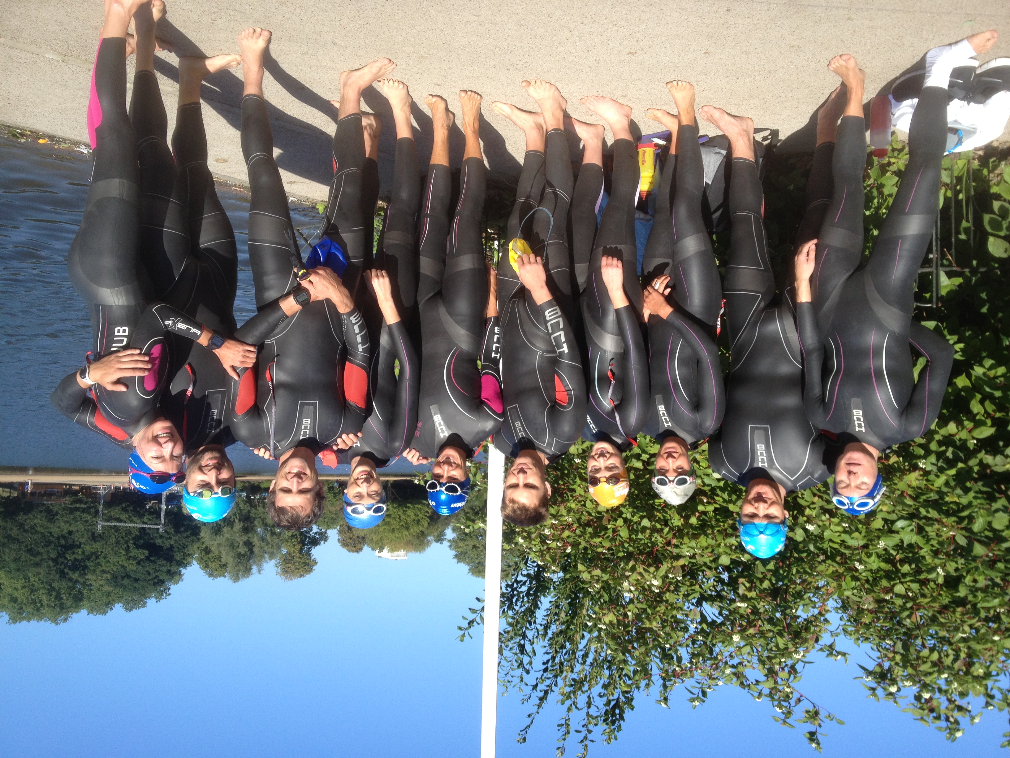 A group of swimmers in wetsuits beside the water
